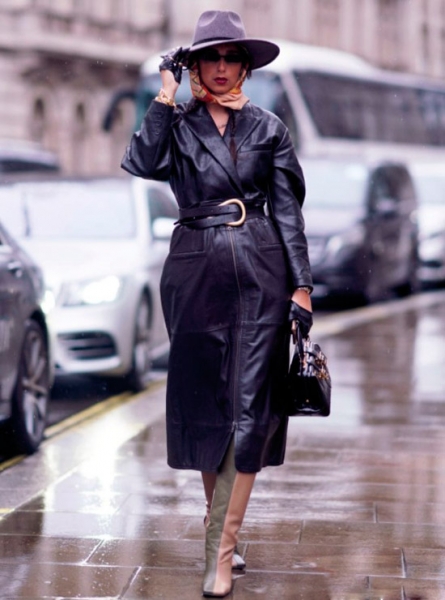Девушка в черном кожаном плаще с поясом, двухцветные сапоги и серая шляпа защищает от дождя