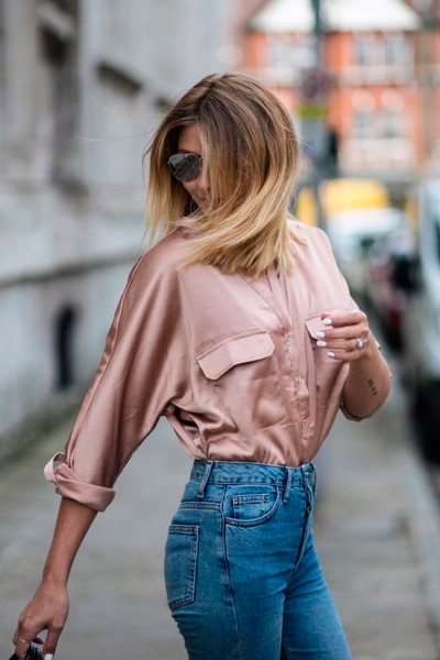 Девушка в простых джинсах с завышенной талией, нежная розовая рубашка из атласа, образ завершают солнцезащитные очки